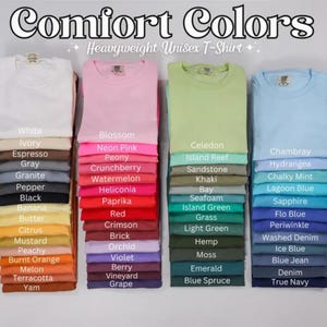 May include: Image of folded Comfort Colors heavyweight unisex t-shirts in various colors. The shirts are stacked in columns, with color names like "White," "Blossom," "Celedon," and "Chambray" displayed below each stack. The image features a variety of shades.