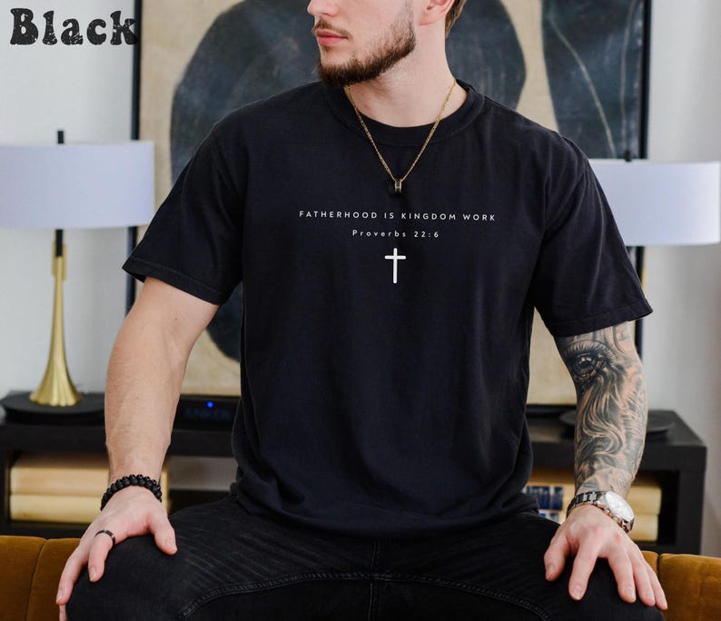 Puede incluir: Camiseta negra con el texto "FATHERHOOD IS KINGDOM WORK" y una cruz blanca. El texto "Proverbios 22:6" est&aacute; debajo. La camiseta es de color negro liso.