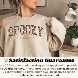 May include: Beige sweatshirt with the text "SPOOKY season" in a black and orange font. The word "SPOOKY" is filled with Halloween-themed patterns. The sweatshirt is made of a soft material.