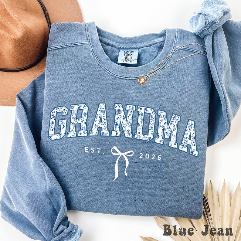 Blue Jean comfort colors sweatshirt with Blue floral toile text "Grandma Est. 2026" and white bow design.