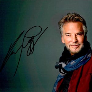 May include: A signed photograph featuring a man with graying hair and a beard, wearing a red jacket and a blue and black scarf. The signature is in black ink on the upper left corner. The background is a gradient of green and gray.