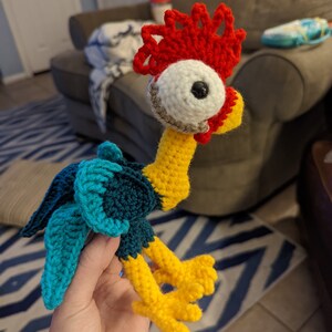May include: A crocheted rooster toy with a red comb, white eye, and black pupil. The rooster is yellow, blue, and green.