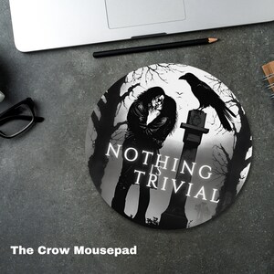 May include: A black and white round mousepad featuring a black crow perched on a tombstone. The crow is looking to the left. The tombstone has the words "Nothing is Trivial" inscribed on it. A couple is standing in front of the tombstone. The background is a dark forest.