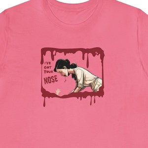 May include: Pink t-shirt with a graphic of a woman with blood dripping from her nose. The graphic is in a red frame with the text "I've got your nose" in white.