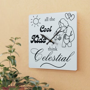 May include: White square clock with black hands and a black design. The design includes a sun, two hearts, a person holding a child, and the text "all the Cool Kids think Celestial".