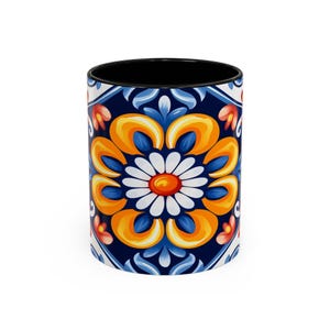 May include: A ceramic mug with a black interior and a colourful floral design. The design features a large yellow flower with a white centre and blue petals, surrounded by smaller orange and red flowers. The background is a dark blue with white accents.