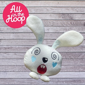 Könnte beinhalten: Ein weißer Plüschhase mit gestickten blauen Augen, einem roten Mund und einer schwarzen Nase. Der Hase hat ein wirbelndes Design auf den Augen und blaue Herzen auf den Wangen.