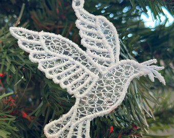 May include: White lace dove ornament hanging on a green Christmas tree. The dove is a symbol of peace and hope.