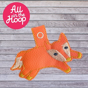 May include: Orange leather fox keychain with a gold embroidered outline and black eyes. The keychain has a metal ring for attaching to a bag or keys.