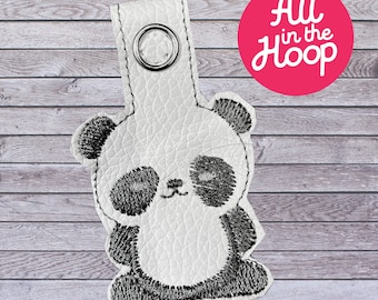 May include: White leather keychain with a black embroidered panda bear design. The keychain has a metal ring for attaching keys.