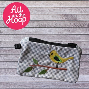 Peut inclure: Une petite pochette zippée en tissu gingham gris et blanc avec une fermeture éclair noire. La pochette est brodée d'un oiseau jaune avec des accents verts assis sur une branche brune avec des feuilles vertes.