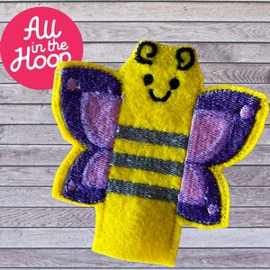 May include: A yellow felt finger puppet with a smiling face, black eyes, and gray stripes. The puppet has purple butterfly wings.