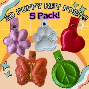 May include: Five 3D puffy key fobs in a 5 pack. The key fobs are shaped like a flower, paw print, heart, butterfly, and peace sign. The key fobs are made of a soft, textured material and are available in a variety of colors.