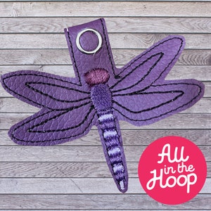 May include: Purple felt dragonfly keychain with a silver ring. The dragonfly has a striped body and detailed wings.