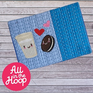 May include: A blue and light blue quilted fabric square with an embroidered image of a glass of milk and a chocolate chip cookie. The milk and cookie have smiling faces and there are two pink hearts above them. The text "All in the Hoop" is on a pink circle in the bottom left corner of the image.