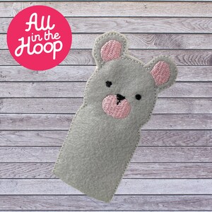 May include: Grey felt finger puppet shaped like a bear with pink ears, nose, and eyes. The bear is looking to the right.