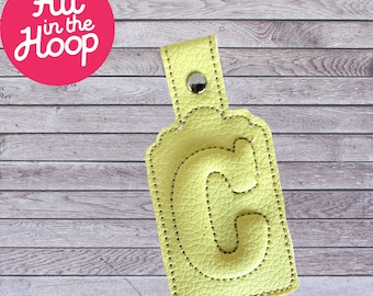 May include: A yellow leather keychain with a stitched letter C on a wood background.