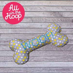 Könnte beinhalten: Ein grauer und weißer Hundeknochen mit gelben Punkten und dem Wort "WOOF!" in Blau gestickt.