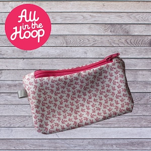 Peut inclure: Une petite pochette zippée rose avec un fond blanc et un motif floral rouge. La pochette est en tissu et possède une fermeture éclair. La pochette est posée sur une surface en bois.