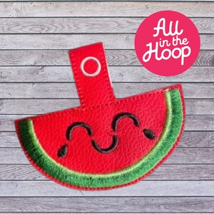 May include: A red and green watermelon slice with a smiling face, embroidered on a fabric keychain with a metal ring.
