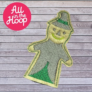 May include: A green and beige felt applique of a smiling scarecrow with a green hat. The scarecrow is wearing a green and beige striped shirt and has a green skirt.