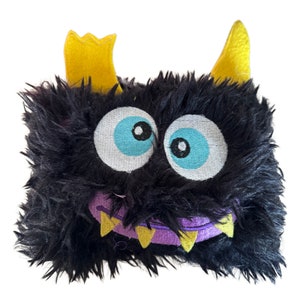 May include: A black plush monster with yellow horns, blue eyes, and a purple mouth with yellow teeth.