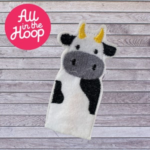 May include: A white cow finger puppet with black spots and yellow horns. The puppet is made of felt and is suitable for children's play.