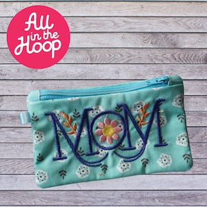 Peut inclure: Une pochette zippée turquoise à motif floral. La pochette est ornée d'un motif brodé qui dit "MOM" avec une fleur et des feuilles.
