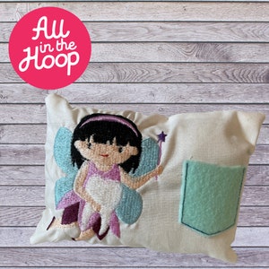 May include: A white pillow with a tooth fairy embroidered on it. The fairy is wearing a purple dress and blue wings. The pillow has a light blue pocket on the right side.