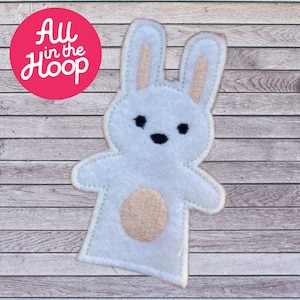 May include: A white felt bunny finger puppet with light pink accents on the ears and belly. The puppet has black eyes and a stitched outline. The text "All in the Hoop" is in a pink circle in the upper left corner.