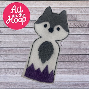 May include: A white felt finger puppet with a gray wolf face and purple felt mountain base. The wolf has black eyes and a black nose.