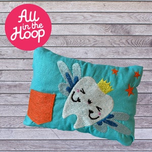 May include: A turquoise pillow with a pocket on the front. The pillow is embroidered with a tooth wearing a crown and wings. The tooth has a happy face and is surrounded by stars.
