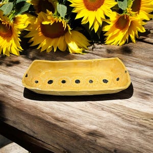 May include: A yellow ceramic serving dish with a row of black sunflower designs around the rim.