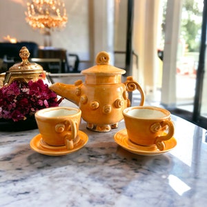 May include: A set of yellow ceramic teacups and teapot with a textured, swirl design. The teapot has a lid and a spout. The cups have handles and saucers.