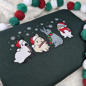 May include: Dark green sweatshirt featuring an embroidered design of four rabbits in festive attire. Each rabbit is wearing a Santa hat or scarf, with snowflakes scattered around them. A candy cane is held by one rabbit. A Christmas-themed design.