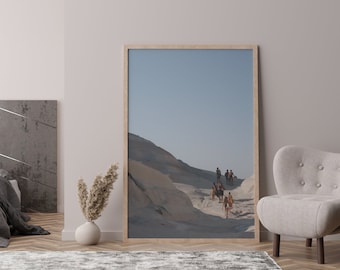 May include: A framed photograph of a group of people walking on a sandy path in a desert landscape. The sky is blue and the sand is a light beige color.