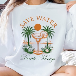 May include: White sweatshirt with the text "Save Water Drink Margs" in orange and green. The graphic features a margarita glass with a lime wedge, palm trees, and a sun.