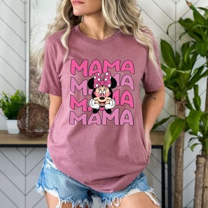 May include: A mauve t-shirt with a graphic of Minnie Mouse wearing sunglasses and a pink bow. The text "MAMA" is repeated four times in pink and white.