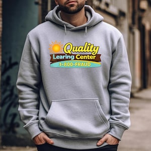 May include: A gray hooded sweatshirt with a large front pocket. The sweatshirt features a graphic with a sun, the words "Quality Learing Center", and the phone number "1-800-FRAUD" in a colorful design.