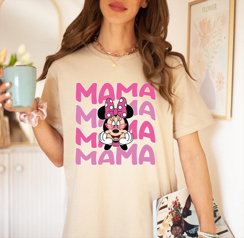 May include: A beige t-shirt with a pink and white graphic of Mickey Mouse's girlfriend Minnie Mouse. The graphic says "MAMA" four times in a stacked design.