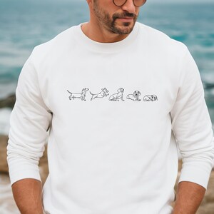 Peut inclure: Sweat-shirt blanc &agrave; manches longues avec un dessin au trait noir de cinq teckels dans diff&eacute;rentes poses.