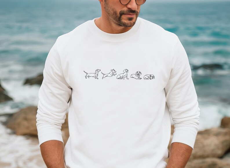 Peut inclure: Sweat-shirt blanc &agrave; manches longues avec un dessin au trait noir de cinq teckels dans diff&eacute;rentes poses.