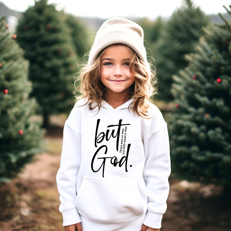 May include: A white hoodie featuring the words "but God" in black script. The hoodie also has the text "There was no way, But God made a way." The person in the image is wearing a beige beanie.