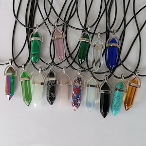 Könnte beinhalten: Eine Sammlung von 17 Kristallspitzenanhängern an schwarzen Schnüren. Die Anhänger bestehen aus verschiedenen Kristallarten, darunter klarer Quarz, Amethyst, Rosenquarz und grüner Aventurin. Die Anhänger sind alle etwa 5 cm lang.