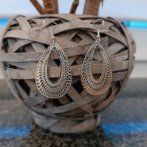 Könnte beinhalten: Ein Paar silberne Ohrhänger mit einem filigranen, komplizierten Design. Die Ohrringe sind tropfenförmig mit einer runden Öffnung in der Mitte.