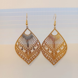 Könnte beinhalten: Ein Paar goldfarbene Ohrhänger mit einem filigranen, komplizierten Design, das mehrere Schichten aus Herzen und Linien aufweist. Die Ohrringe sind leicht und haben einen modernen, bohemian Stil.