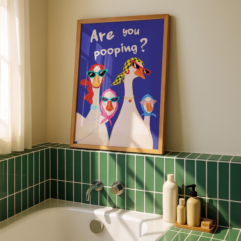 May include: A framed art print featuring three geese wearing sunglasses and scarves, set against a blue background. The text "Are you pooping?" is displayed in white. The artwork is in a bathroom setting, with green tiles and bath accessories.