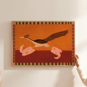 Peut inclure: Une impression rectangulaire encadrée représentant un grand géocoucou au corps brun foncé tacheté et à la longue queue, portant des bottes de cow-boy roses ornées d'étoiles jaunes. Le fond est orange et rouge foncé avec une bordure de cactus verts.