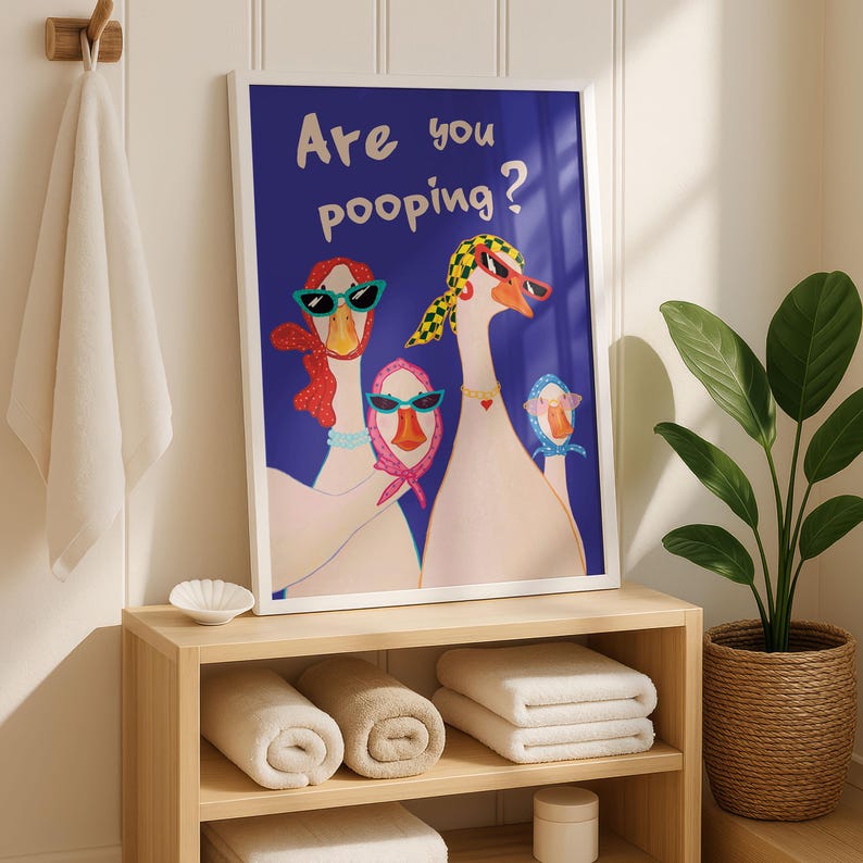 May include: A framed art print featuring a whimsical illustration of three geese wearing sunglasses and scarves against a deep blue background. The text "Are you pooping?" is written above the geese. The print is displayed in a bathroom setting.