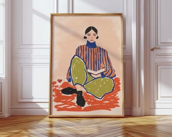 Peut inclure: Une affiche encadrée représente une personne assise en tailleur, lisant un livre. La personne porte un haut rayé bleu et orange et un pantalon vert. Un verre de vin rouge est à proximité. L'œuvre est sur fond pêche.